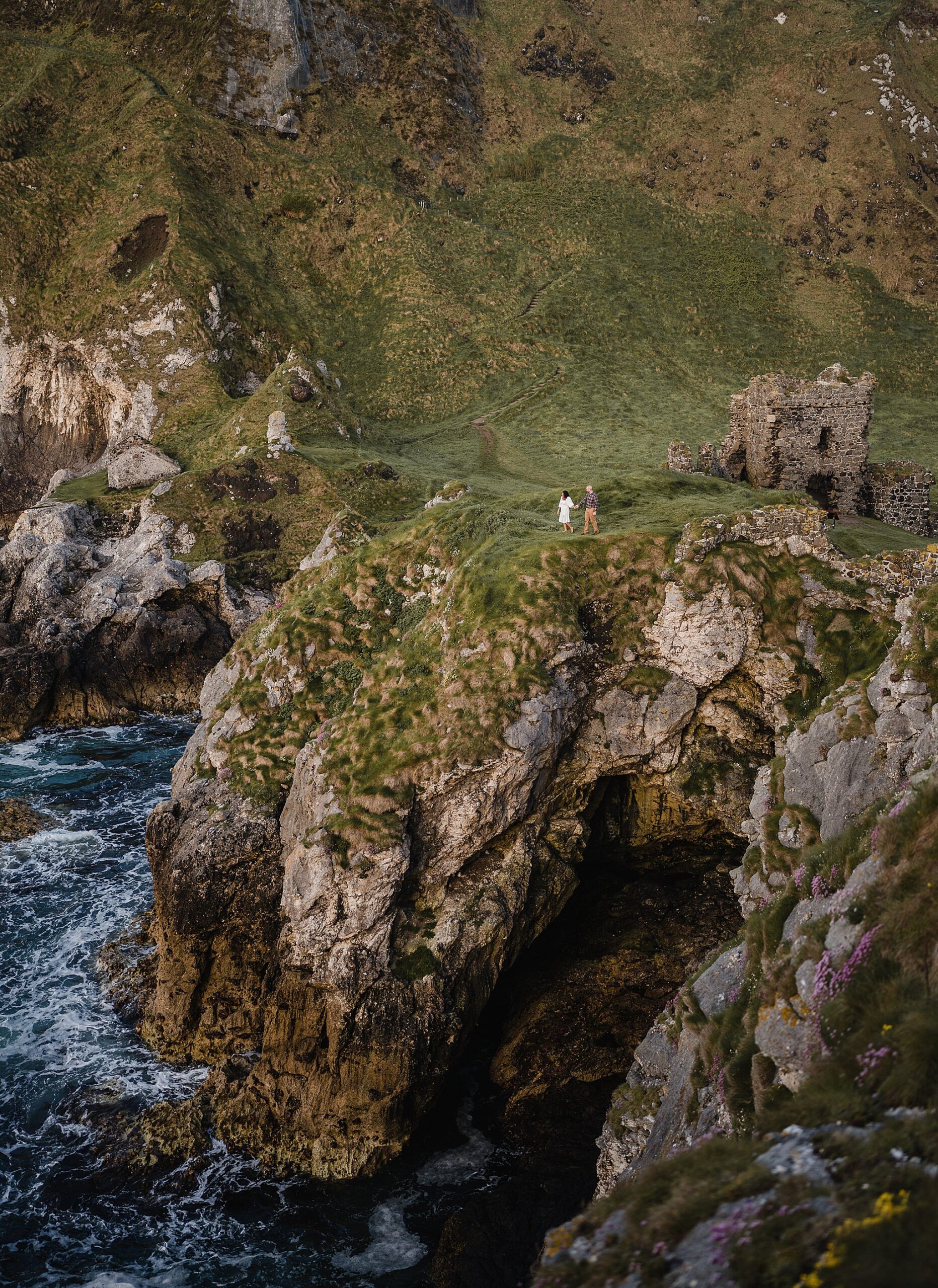 couple walking along cliff edge at kinbane castle at sunrise